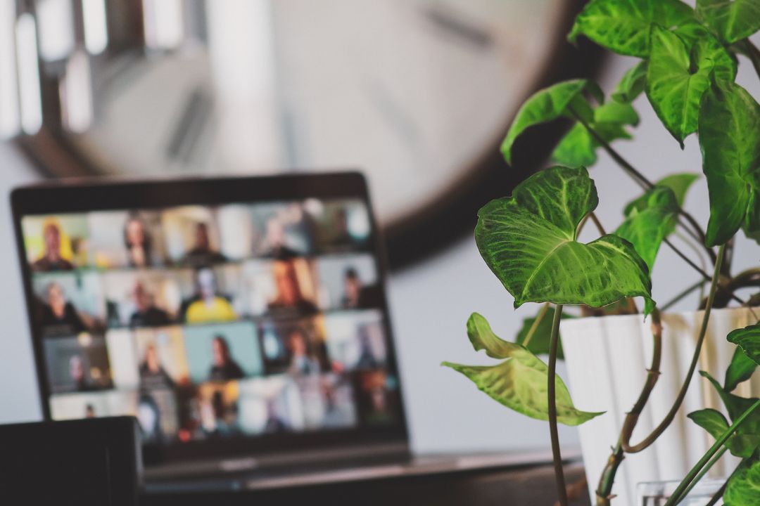 Laptop showing a grid of video meeting participants in front of a large wall clock