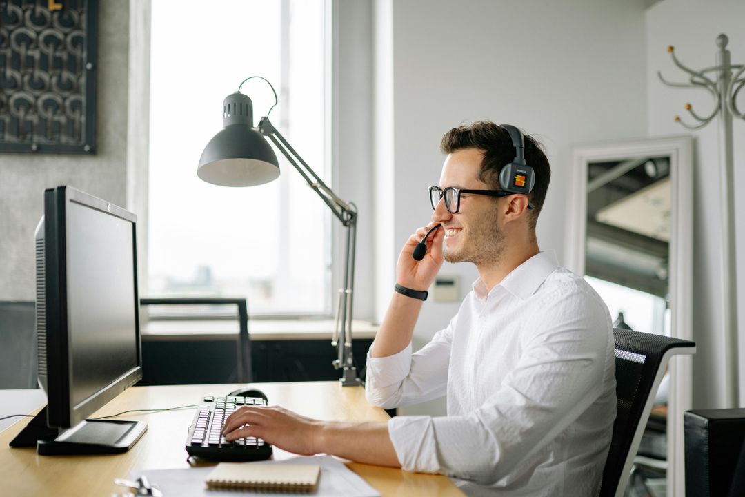 Employee smiling during a one-on-one check-in call at an office desk with a headset